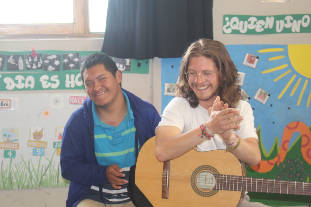 Een vrijwilliger speelt gitaar samen met een leerling met het syndroom van down.